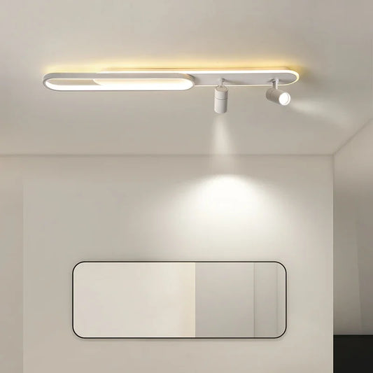 White linear ceiling lamp with an oval accent and two spotlight fixtures casting light downwards onto a rectangular mirror below.