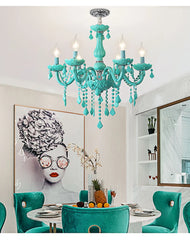 A cyan crystal chandelier hanging above a dining table set with teal velvet chairs, in a room with modern artwork.