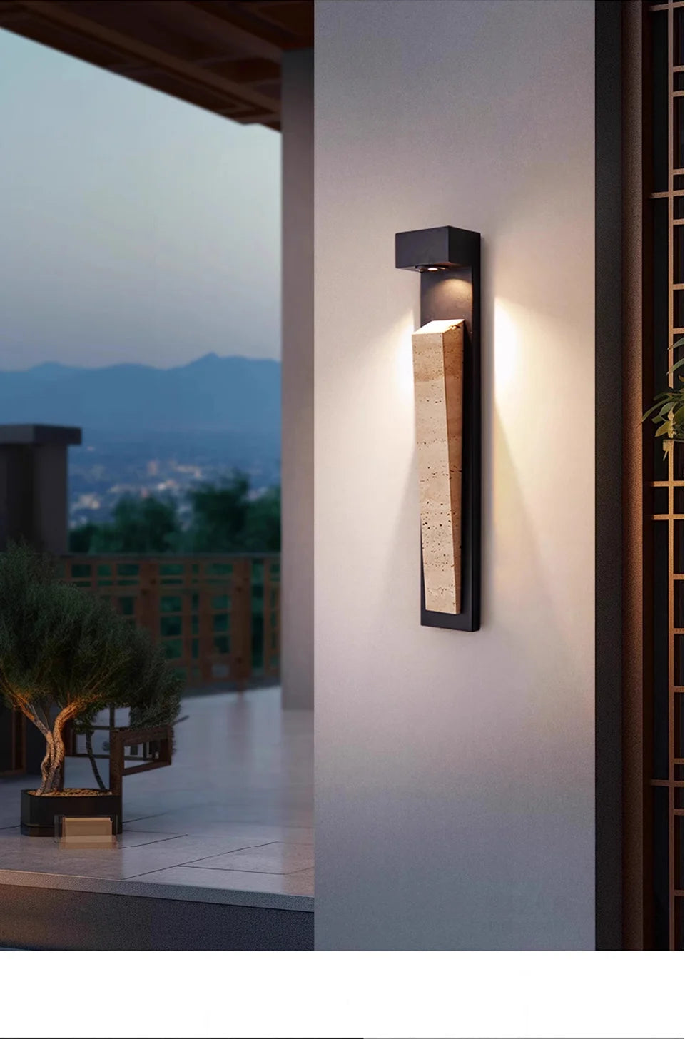 A modern black wall sconce with natural stone detail mounted on an outdoor wall with a view of a city at dusk.