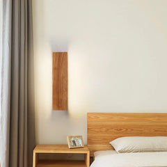 Wooden wall sconce mounted on a white wall next to a bed with curtains and a wooden nightstand with a picture frame.