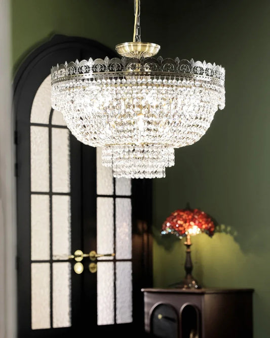 Tiered crystal waterfall chandelier with polished chrome frame hanging in a room with a dark arched doorway and green walls.