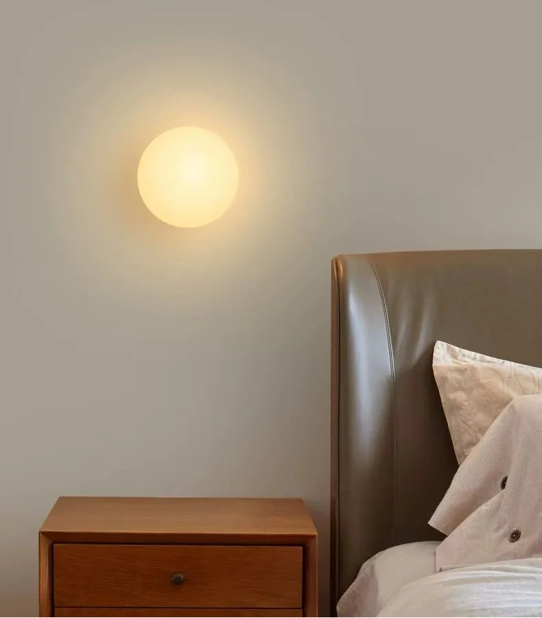 Wall-mounted light fixture on a neutral wall next to a bed and nightstand.