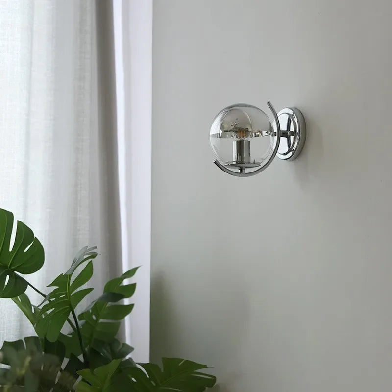 Modern wall sconce with glass shade on a white wall next to a plant