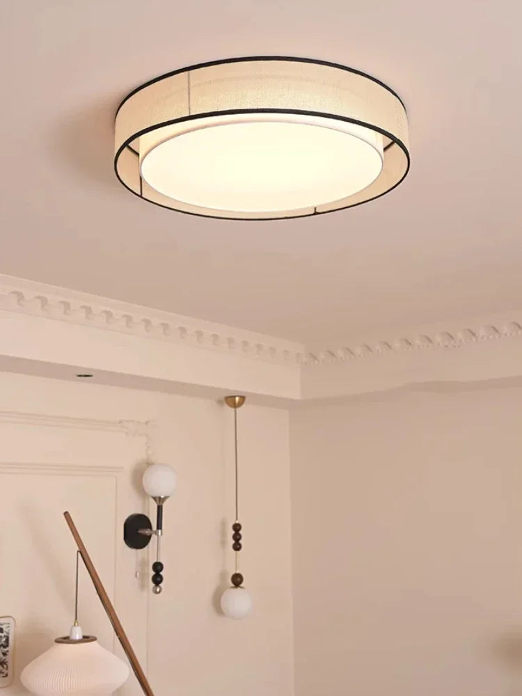 A residential interior with a beige fabric drum flush mount ceiling light illuminated, showing decorative ceiling molding.