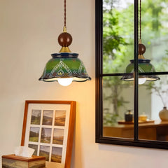 Close-up of the green ceramic bell pendant light showing intricate hand-painted floral patterns and scalloped edge, reflecting in a window.