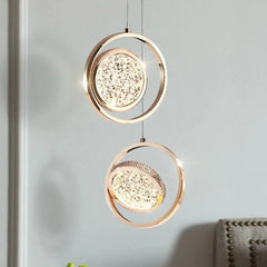 Two gold ring pendant lights with crystal diffusers hanging against a grey wall.