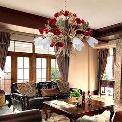 A gold floral pendant light with red rose buds and frosted glass shades suspended above a dark leather sofa and a wooden coffee table in a living room.