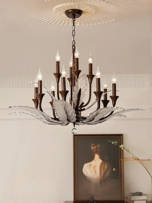 A large bronze chandelier with multiple candle-style lights and metal leaf accents, installed in a room with blinds.