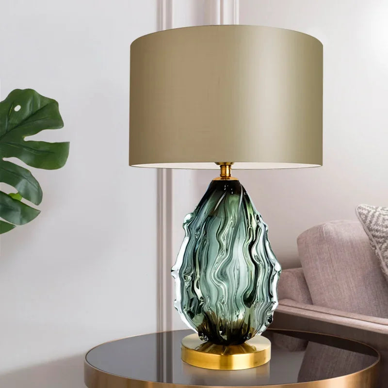 Decorative table lamp with green glass base and beige shade on a round table.
