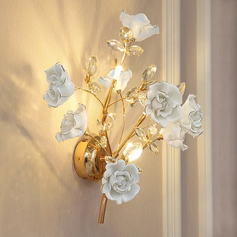 A gold wall sconce with multiple white floral accents and clear crystal details, mounted on a textured wallpaper.
