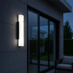 A modern wall sconce with a marble-effect diffuser mounted on a dark facade next to a large glass sliding door.