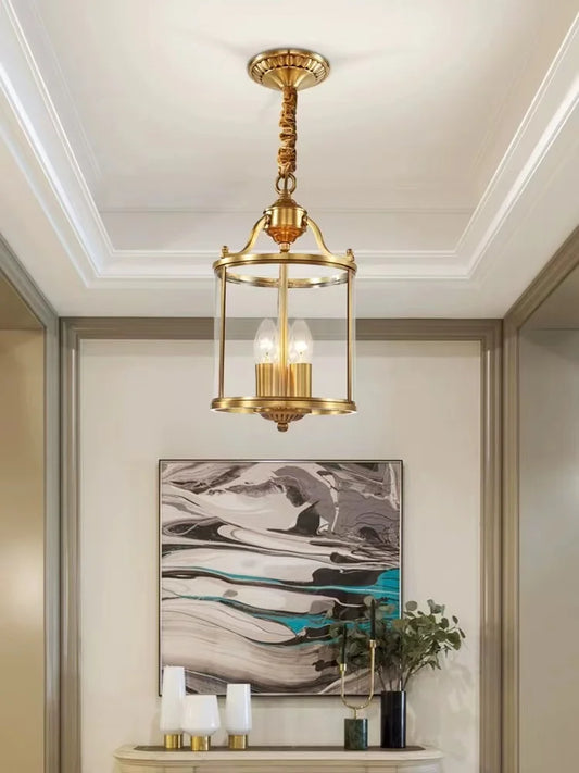 Gold lantern pendant light with clear glass shade hanging from a ceiling with a decorative chain.