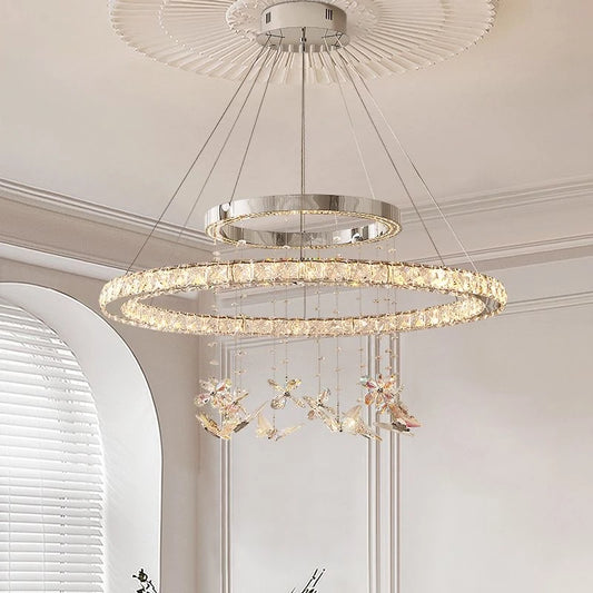 Close-up of a multi-tiered ring chandelier with numerous clear K9 crystals and decorative butterfly-shaped ornaments hanging below, illuminated against a white ceiling.