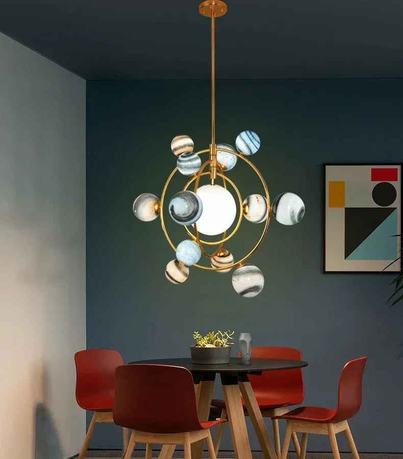 Modern chandelier hanging above a dining table with red chairs in a room with a dark wall and abstract art.