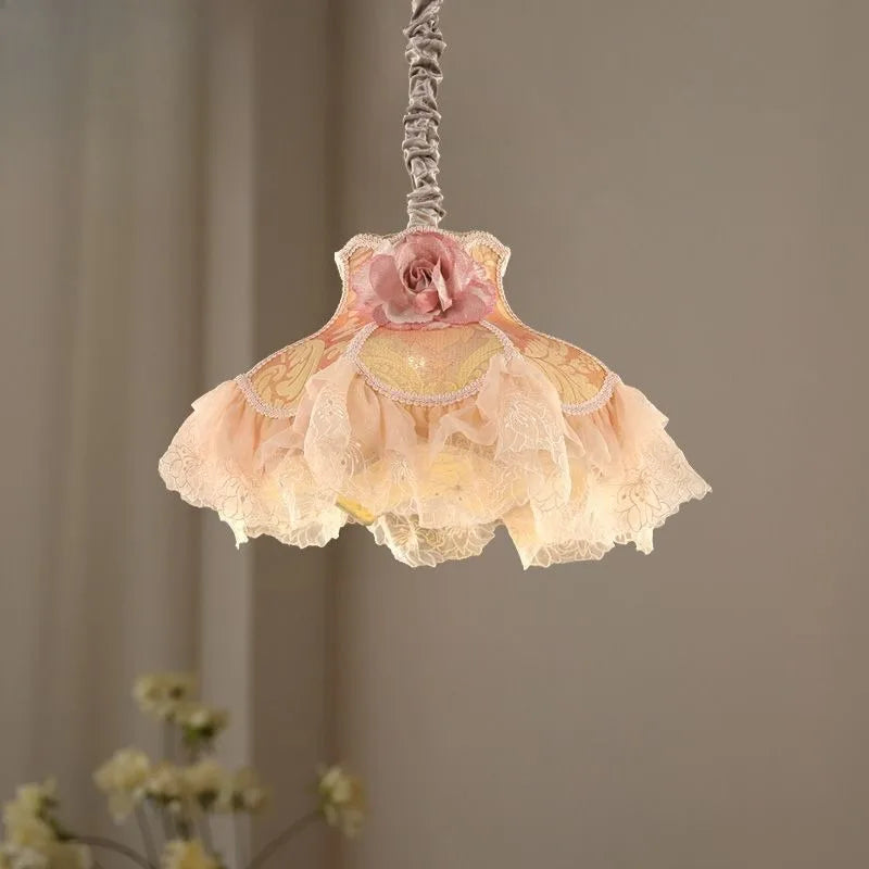 Side view of a fabric pendant light featuring a pink rose and layered, ruffled fabric shades emitting a warm glow.