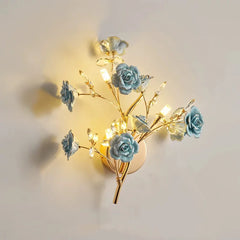A gold wall sconce with blue ceramic flowers and clear crystals, emitting a warm light.