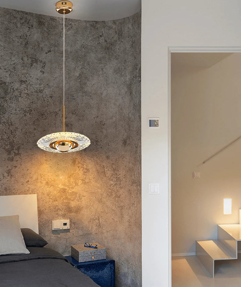 Modern pendant light in a bedroom with concrete wall and bed in the foreground.