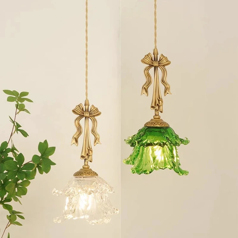 Two hanging light fixtures with gold bows and green glass against a neutral background.