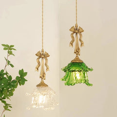 Two hanging light fixtures with gold bows and green glass against a neutral background.