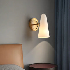 Wall-mounted lamp with a cone-shaped white shade on a gray wall next to a bed.