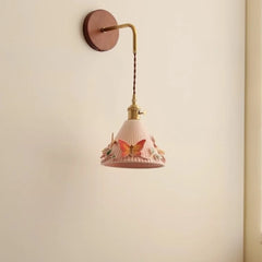 Wall-mounted lamp with pink shade and butterfly design on a beige wall