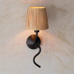 Wall-mounted lamp with a pleated beige shade and black curved arm on a textured wall.