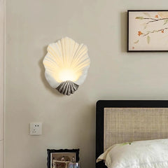 Shell-shaped wall lamp on a wall above a bed with a framed picture.