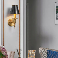 Wall-mounted lamp with black shade and gold base in a room setting.