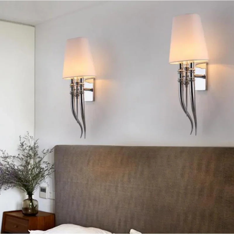 Two wall sconces with lampshades on a wall above a bed.