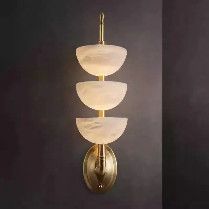 Wall-mounted light fixture with three tiered glass shades on a dark background