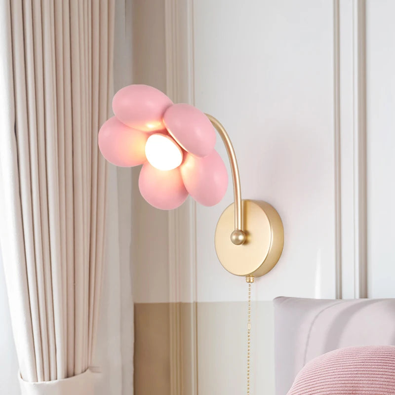 Pink flower-shaped wall lamp with gold arm on a neutral background