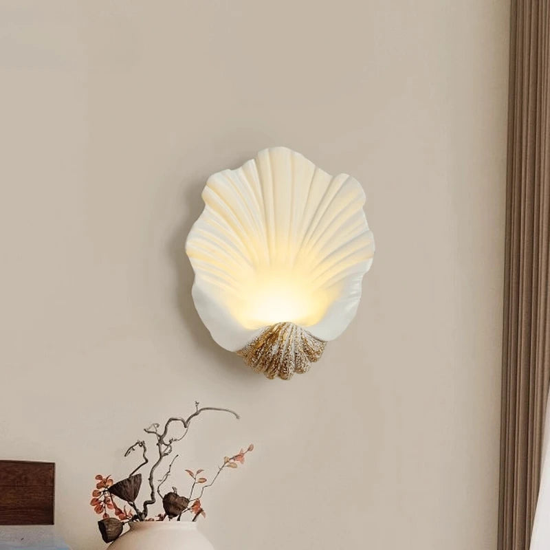 Shell-shaped wall lamp on a beige wall with a decorative item below.