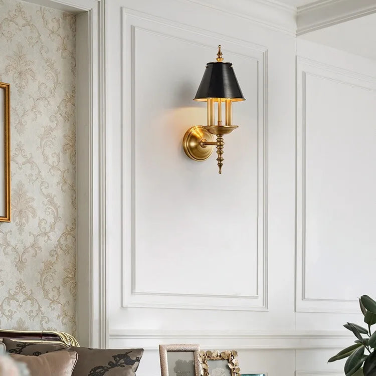 Decorative wall sconce with gold fixture and black shade on a white paneled wall.