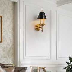 Decorative wall sconce with gold fixture and black shade on a white paneled wall.