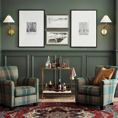 Living room with plaid armchairs, a coffee table, and framed pictures on a green paneled wall.