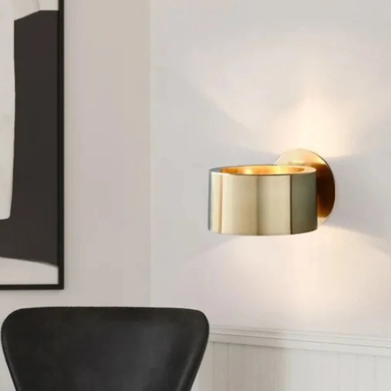 Gold wall sconce on a white wall with a black chair in the foreground