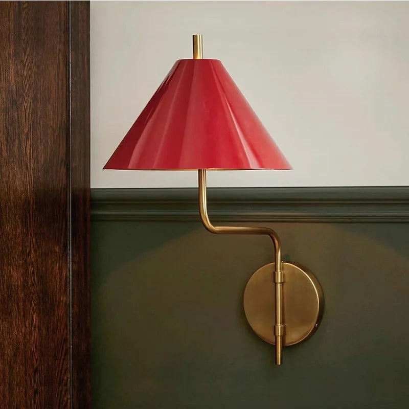 Wall-mounted lamp with red shade and gold fixture on a green wall.