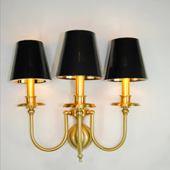 Three-arm wall sconce with black lampshades and gold metal finish on a white background