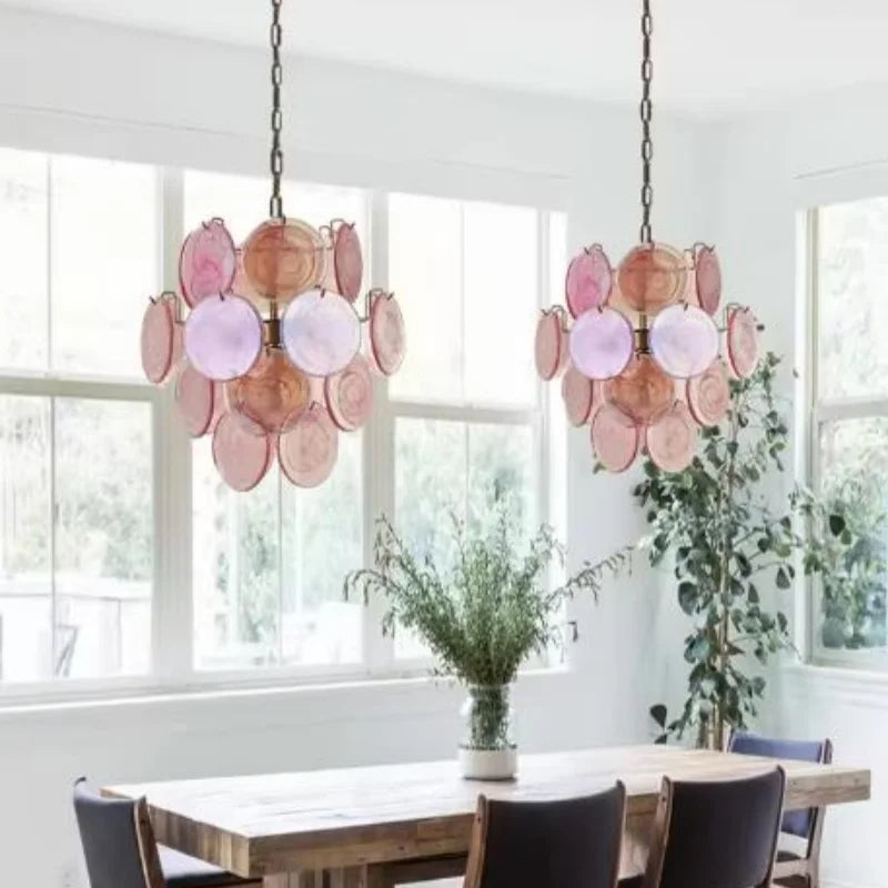 Modern chandelier with pink and orange disc design hanging above a dining table in a bright room. Liglite vintage stained glass chandelier for statement lighting.