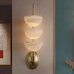 Wall-mounted light fixture with three tiered glass shades on a neutral wall.