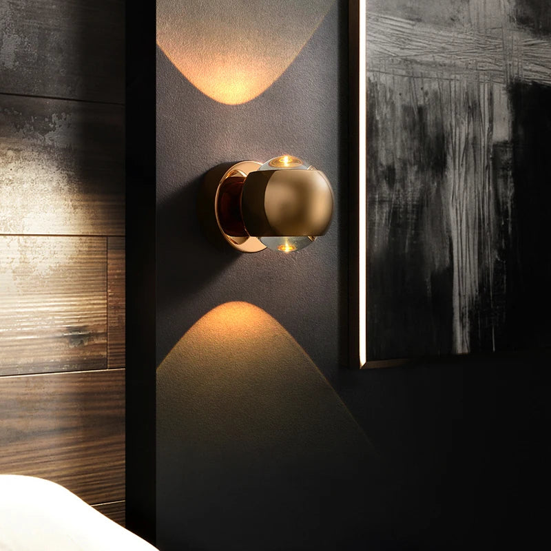 Wall-mounted gold light fixture on a dark wall with abstract art.