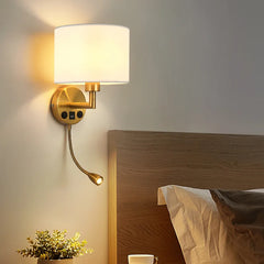 Wall-mounted lamp with a white shade and gold base next to a wooden headboard.