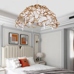 Gold chandelier hanging above a bed in a bedroom with white walls and decorative pillows.