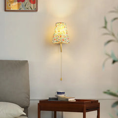 Decorative wall lamp with colourful shade on a wall next to a wooden side table with books and a cup. Modern wood and fabric bedside wall sconce with E27 base.