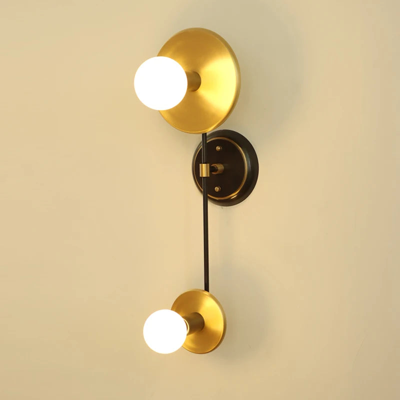Gold wall sconce with two light bulbs on a beige wall