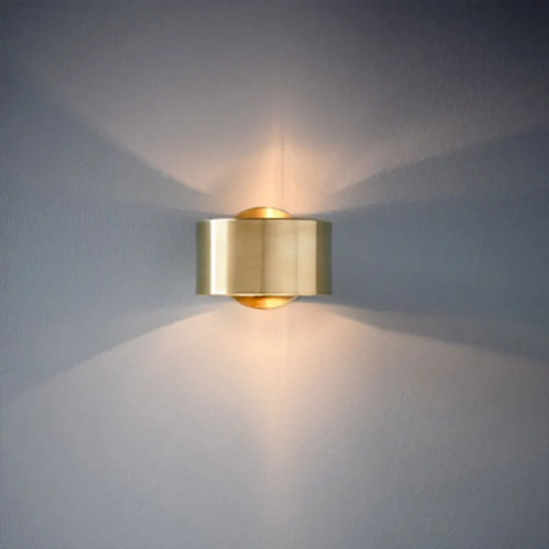 Gold wall-mounted light fixture casting a warm glow on a gray wall.