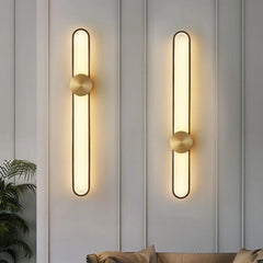 Two modern wall lights on a gray paneled wall with a plant and sofa in the background.