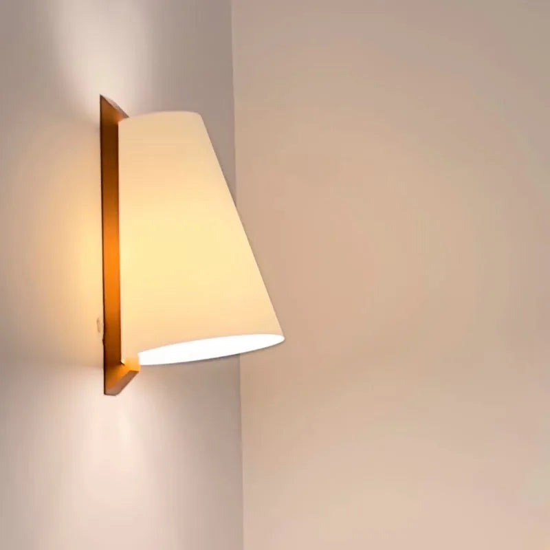 Wall-mounted light fixture with a beige shade on a plain wall.