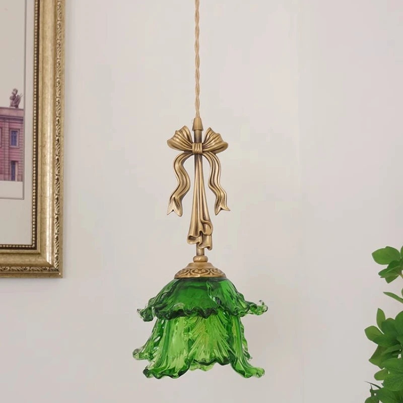 Decorative pendant light with green glass shade and gold fixture on a white wall.