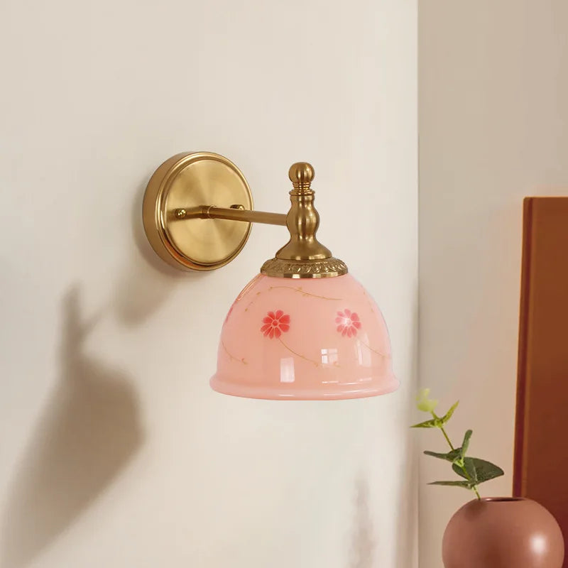 Wall-mounted lamp with pink glass shade and gold fixture on a light beige wall.